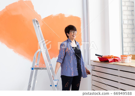 Pretty middle-aged woman with painting roller indoors. Redecoration, renovation, apartment repair and refreshment concept. Pretty middle-aged woman with painting roller indoors. Redecoration, renovation, apartment repair and refreshment concept. 66949588