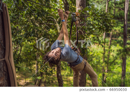 Young attractive man in adventure rope park in safety equipment Young attractive man in adventure rope park in safety equipment 66950030