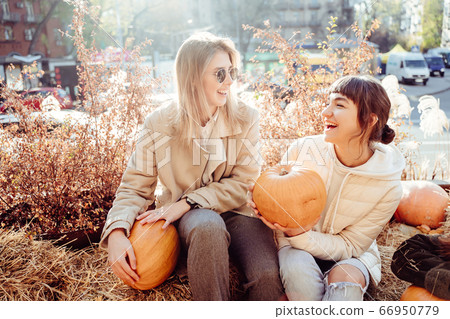 Girls holds pumpkins in hands on the background of the street. Girls holds pumpkins in hands on the background of the street. 66950779