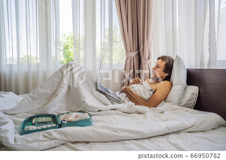 Male patient is sick while lying in his bed and calls an online doctor through a gadget Male patient is sick while lying in his bed and calls an online doctor through a gadget 66950782