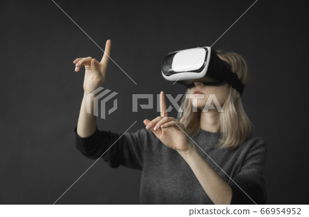 Young woman wearing virtual reality goggles headset, vr box. Connection, technology, new generation, progress concept. Girl trying to touch objects in virtual reality. Young woman wearing virtual reality goggles headset, vr box. Connection, technology, new generation, progress concept. Girl trying to touch objects in virtual reality. 66954952