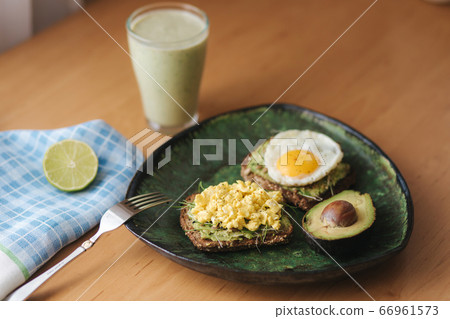 Different cooked egg on avocado sandwich with whole grain bread on wooden board. Smoothie with spinach 66961573