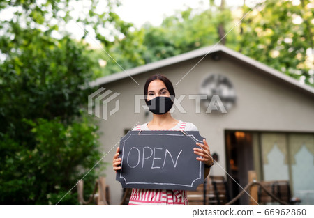 Young woman with face mask working in cafe, holding open sign. Young woman with face mask working in cafe, holding open sign. 66962860