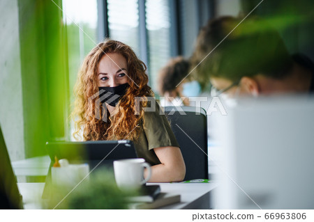 Young woman with face mask back at work in office after lockdown. 66963806