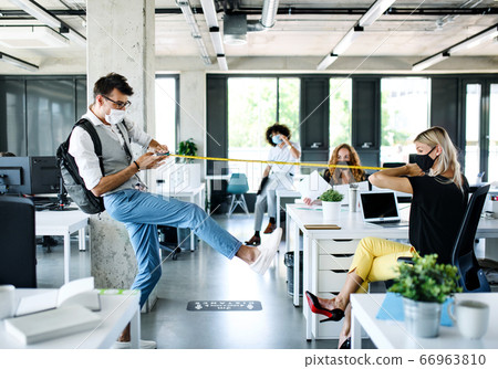 Young people with face masks back at work in office after lockdown, measuring distance. Young people with face masks back at work in office after lockdown, measuring distance. 66963810