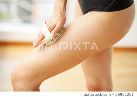 Woman's arm holding dry brush to top of her leg, cellulite treatment and dry brushing. 66965261