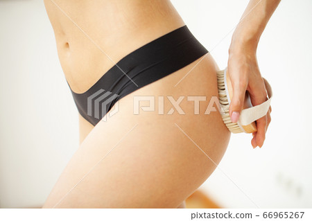Woman's arm holding dry brush to top of her leg, cellulite treatment and dry brushing. 66965267