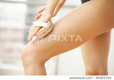 Woman's arm holding dry brush to top of her leg, cellulite treatment and dry brushing. Woman's arm holding dry brush to top of her leg, cellulite treatment and dry brushing. 66965268