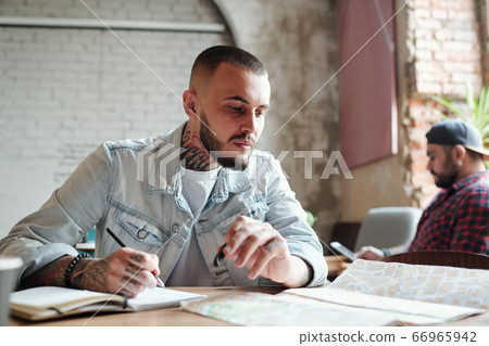 Tattooed guy analyzing route with map Tattooed guy analyzing route with map 66965942