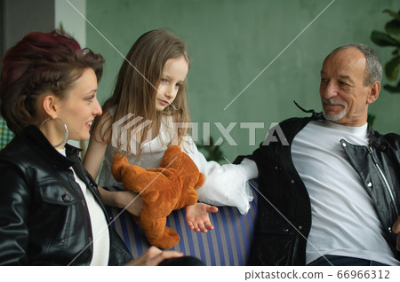 Family portrait of adult daughter, little granddaughter and senior grandfather in loft room with houseplants. Man and woman are wearing black leather jackets in punk style, generation concept Family portrait of adult daughter, little granddaughter and senior grandfather in loft room with houseplants. Man and woman are wearing black leather jackets in punk style, generation concept 66966312