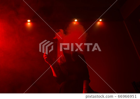 Girl model smokes vape in red light. Girl model smokes vape in red light. 66966951