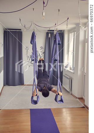 Athletic man using blue hammock swing for aerial yoga Athletic man using blue hammock swing for aerial yoga 66970372
