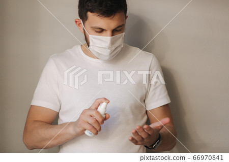 Young man in protective mask use satitizer at home. Man use disinfector. Quarantine at home. Coronavirus theme. Stay at home 66970841