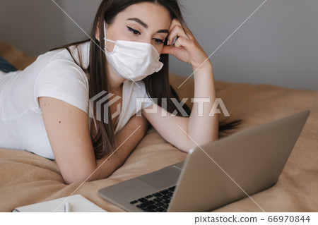 Young woman in mask use laptop on the bed. Female working during quarantine in bedroom. Student study at home. Stay at home Young woman in mask use laptop on the bed. Female working during quarantine in bedroom. Student study at home. Stay at home 66970844