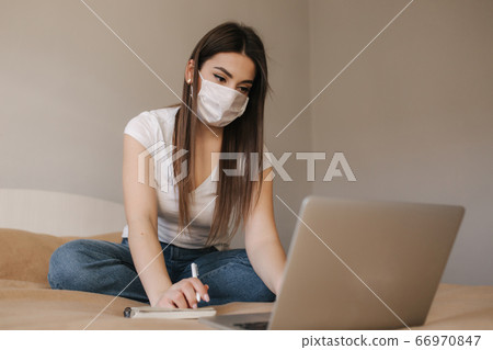 Young woman in mask use laptop on the bed. Female working during quarantine in bedroom. Student study at home. Stay at home 66970847