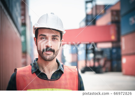 Portrait of Confident Transport Engineer Man in Safety Equipment Standing in Container Ship Yard.  66972826