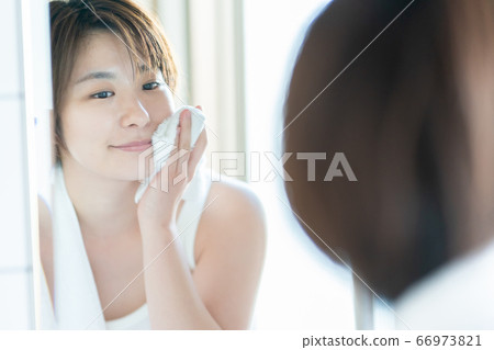 Woman in her 30s wiping her face with a towel after washing her face Woman in her 30s wiping her face with a towel after washing her face 66973821