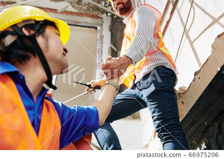 Construction worker helping colleague Construction worker helping colleague 66975206