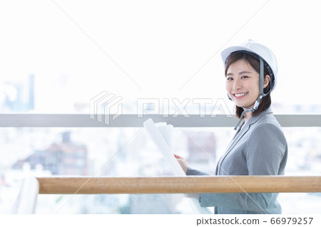 Business woman wearing a helmet and looking at the drawing Business woman wearing a helmet and looking at the drawing 66979257