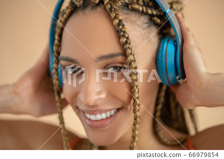 Smiling young African American female touching blue headphones, listening to music Smiling young African American female touching blue headphones, listening to music 66979854