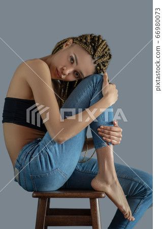 Sad young African American sitting on chair, putting her head on knee Sad young African American sitting on chair, putting her head on knee 66980073