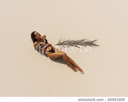 Top Aerial Drone View of Woman in Swimsuit Bikini Relaxing and Sunbathing on Beach 66981800