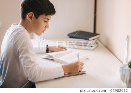 Young boy sitting at desk read the book and write down in notebook. Study at home during quarantine 66982612