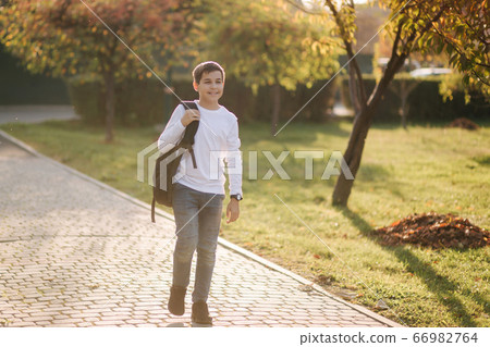 Happy schoolboy go back home after lessons. Teenager in white shirt denim jeans with backpack Happy schoolboy go back home after lessons. Teenager in white shirt denim jeans with backpack 66982764