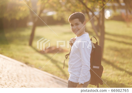 Back view of schoolboy go back home after lessons. Teenager in white shirt denim jeans with backpack 66982765