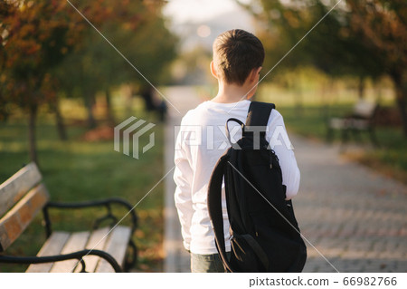 Back view of schoolboy go back home after lessons. Teenager in white shirt denim jeans with backpack 66982766