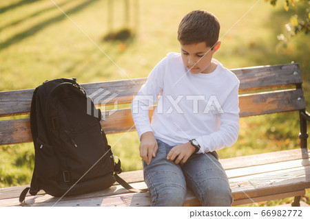 Young boy take out of his pocket smartphone. Teenage boy sitting on the bench in the park Young boy take out of his pocket smartphone. Teenage boy sitting on the bench in the park 66982772