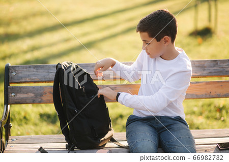 Handsome teenage boy take from his backpack powerbark for charging smarphone. Cute boy in the park in autumn time Handsome teenage boy take from his backpack powerbark for charging smarphone. Cute boy in the park in autumn time 66982782