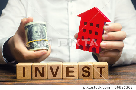 A man with dollars and a house figurine and the word Invest. Real estate financial investment. Favorable investment climate, cheap housing and low demand. Saving savings in a crisis. Rental business 66985302