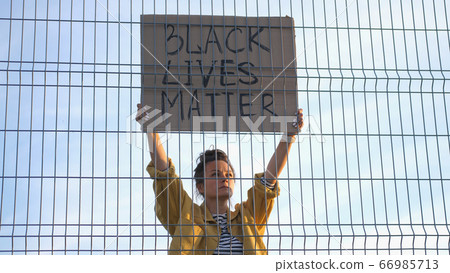Young protesting woman standing behind the fence holds a poster - Black Lives Matter 66985713