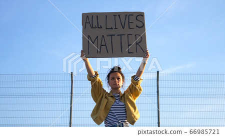Young protesting woman holds a poster over her head - All Lives Matter Young protesting woman holds a poster over her head - All Lives Matter 66985721