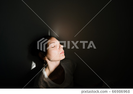 Girl sitting alone in sunlight pocket in dark room. mental health concept 66986968