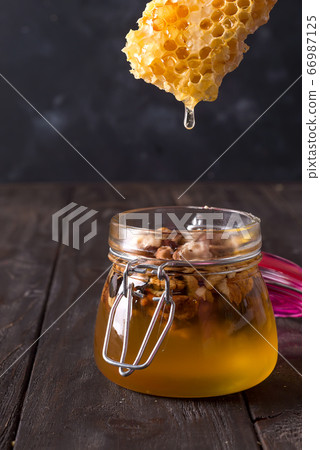 honey comb dripping from dipper into jar with nuts 66987125