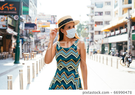 20s Hispanic Brunette woman in a protective mask wear summer sleeveless summ dress in Asia. 20s Hispanic Brunette woman in a protective mask wear summer sleeveless summ dress in Asia. 66990478