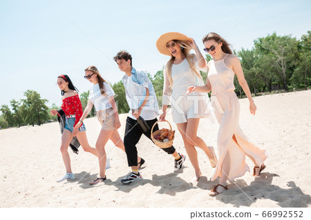 Seasonal feast at beach resort. Group of friends celebrating, resting, having fun on the beach in sunny summer day Seasonal feast at beach resort. Group of friends celebrating, resting, having fun on the beach in sunny summer day 66992552
