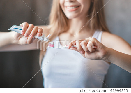 Closeup of young girl applying toothpaste from tube onto brush in bathroom Closeup of young girl applying toothpaste from tube onto brush in bathroom 66994823