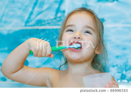 a little girl brushes her teeth and rinses her mouth in the bathroom. portrait of a child with a toothbrush 66996583