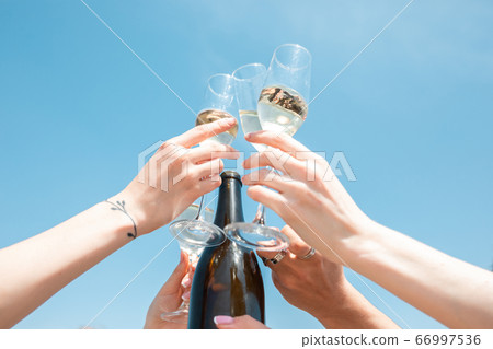 Seasonal feast at beach resort. Close up hands of friends celebrating, resting, having fun, clinking glasses on sky background 66997536