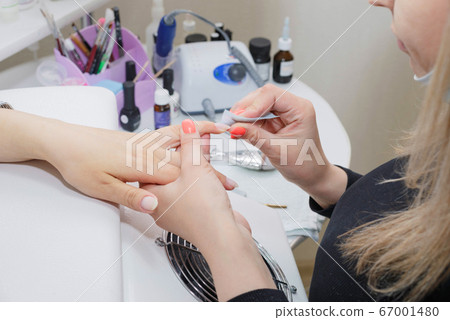 Beautician prepares a nail before applying varnish in a nail salon. Beautician prepares a nail before applying varnish in a nail salon. 67001480