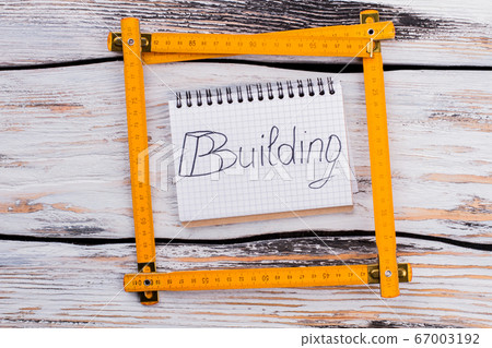Yellow plastic carpenter ruler square on white wooden background. Yellow plastic carpenter ruler square on white wooden background. 67003192