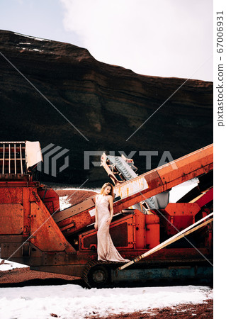 Portrait of a bride model in a golden wedding evening dress, in a yellow-red sandy quarry, in the crater of a volcano in Iceland, Golden Circle. The bride walks near the career vibrating screen. Portrait of a bride model in a golden wedding evening dress, in a yellow-red sandy quarry, in the crater of a volcano in Iceland, Golden Circle. The bride walks near the career vibrating screen. 67006931