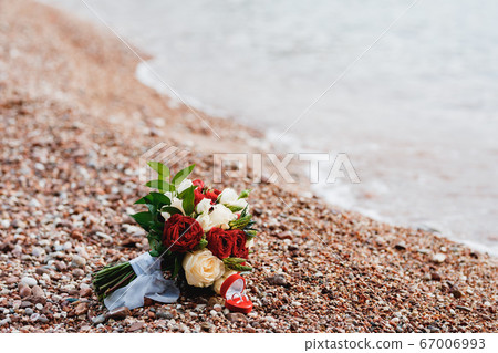 bridal bouquet of white, read and cream roses, ornithogalum, eryngium with white ribbons on the beach near water and wedding rings bridal bouquet of white, read and cream roses, ornithogalum, eryngium with white ribbons on the beach near water and wedding rings 67006993