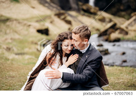 Destination Iceland wedding, near Kvernufoss waterfall. A wedding couple sits on the banks of a mountain river, at a table for a wedding dinner, made of a wooden pallet painted with moss and snags 67007063