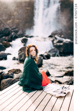 The girl artist paints a picture in the album with watercolors. Near Ehsaraurfoss waterfall, Ehsarau River, Thingvedlir National Park in Iceland. The girl artist paints a picture in the album with watercolors. Near Ehsaraurfoss waterfall, Ehsarau River, Thingvedlir National Park in Iceland. 67007134