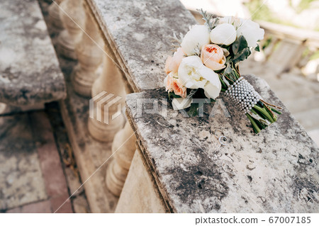 bridal bouquet of white and cream peonies, roses, salal, artemisia with pearl ribbon on the railing of an ancient staircase 67007185