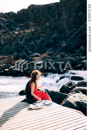 The girl artist paints a picture in the album with watercolors. Near Ehsaraurfoss waterfall, Ehsarau River, Thingvedlir National Park in Iceland. The girl artist paints a picture in the album with watercolors. Near Ehsaraurfoss waterfall, Ehsarau River, Thingvedlir National Park in Iceland. 67007239